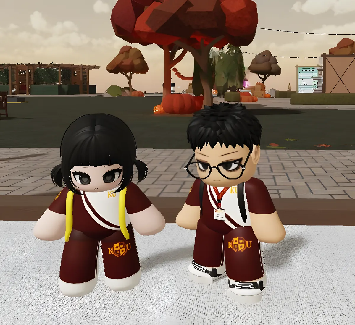 Two members in maroon KU tracksuits in an autumn town square